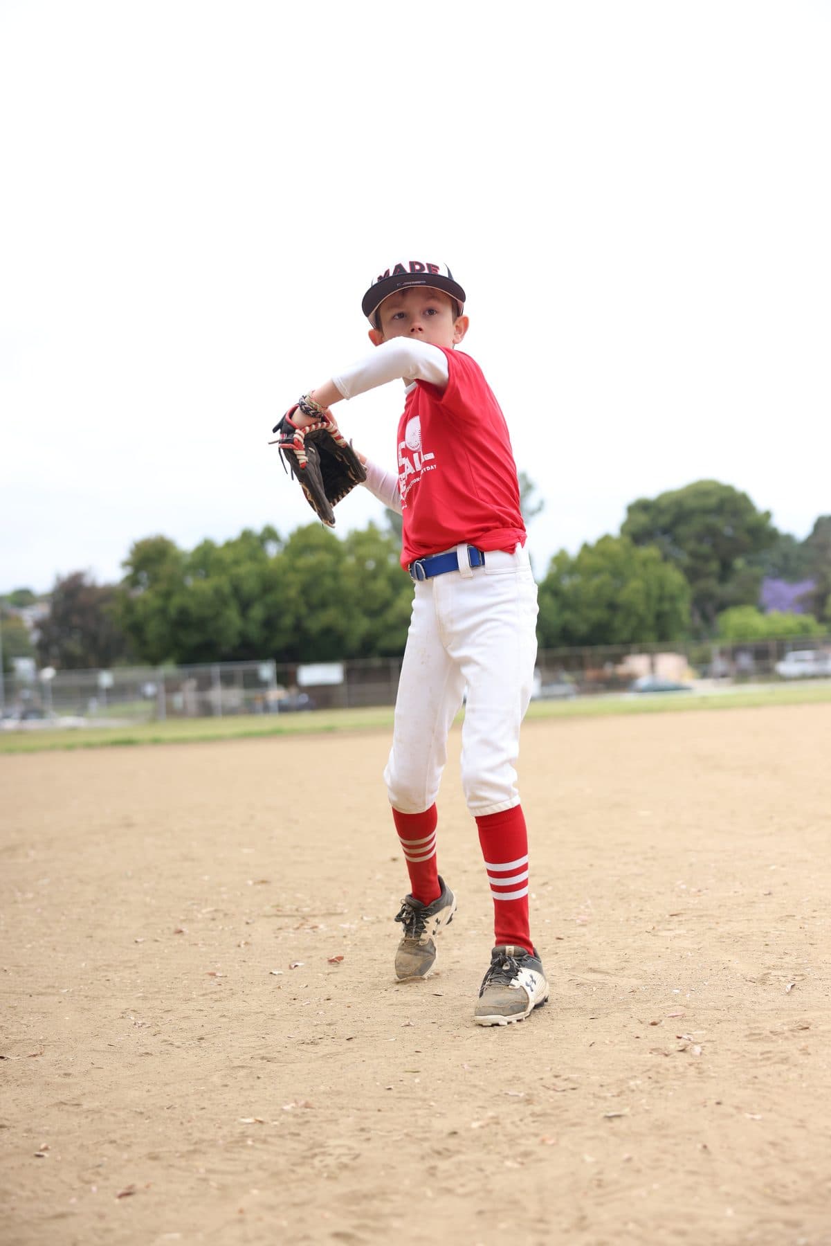 A young pitcher in a red MADE shirt winding up with his glove raised